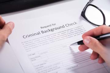 A person with a light skin tone filling out a Request for Criminal Background Check form